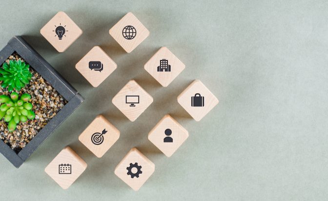 Business concept with wooden blocks with icons, green plant on sage color background flat lay. copy space for text. horizontal image